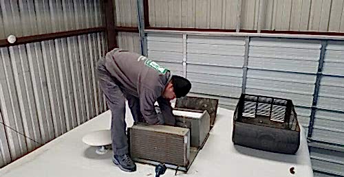 rv mechanic standing on top of a camper working on the air conditioner
