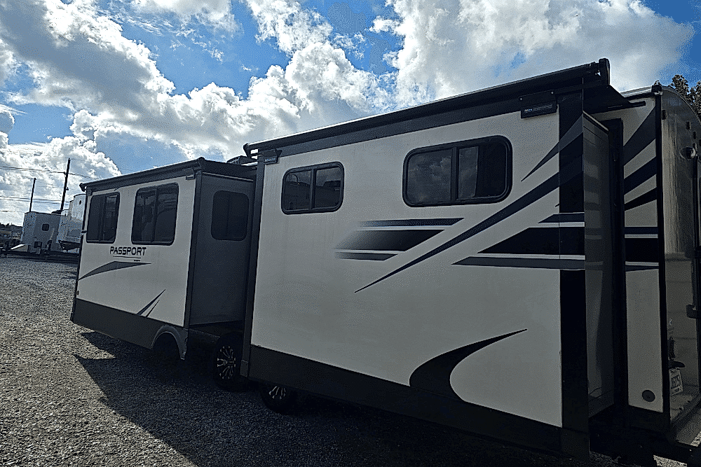 Slide-Out Roof Maintenance, RV repair in Laplace, LA at RV Masters. White Passport travel trailer with extended slide-outs parked under a partly cloudy sky at an RV lot.